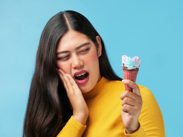 mujer-asiatica-lastimo-sus-dientes-helado-fondo-azul_1286-2461 Mujer comiendo un helado, l que según los consejos de dentistas genera sensibilidad dental